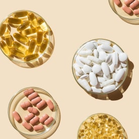 Various pills and capsules, vitamins and dietary supplements in petri dishes on a beige background.